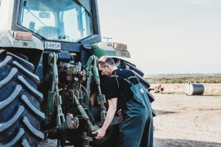 Man in farming waterproof bib and brace fixing a tractor